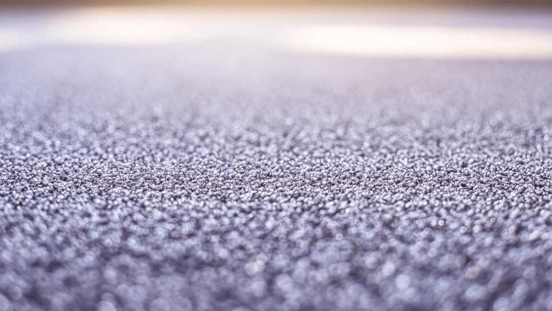 Gros plan d’un tapis avec une texture granuleuse et un effet légèrement brillant, illustrant une surface potentiellement collante en raison de résidus de nettoyage ou d’accumulation de poussière.